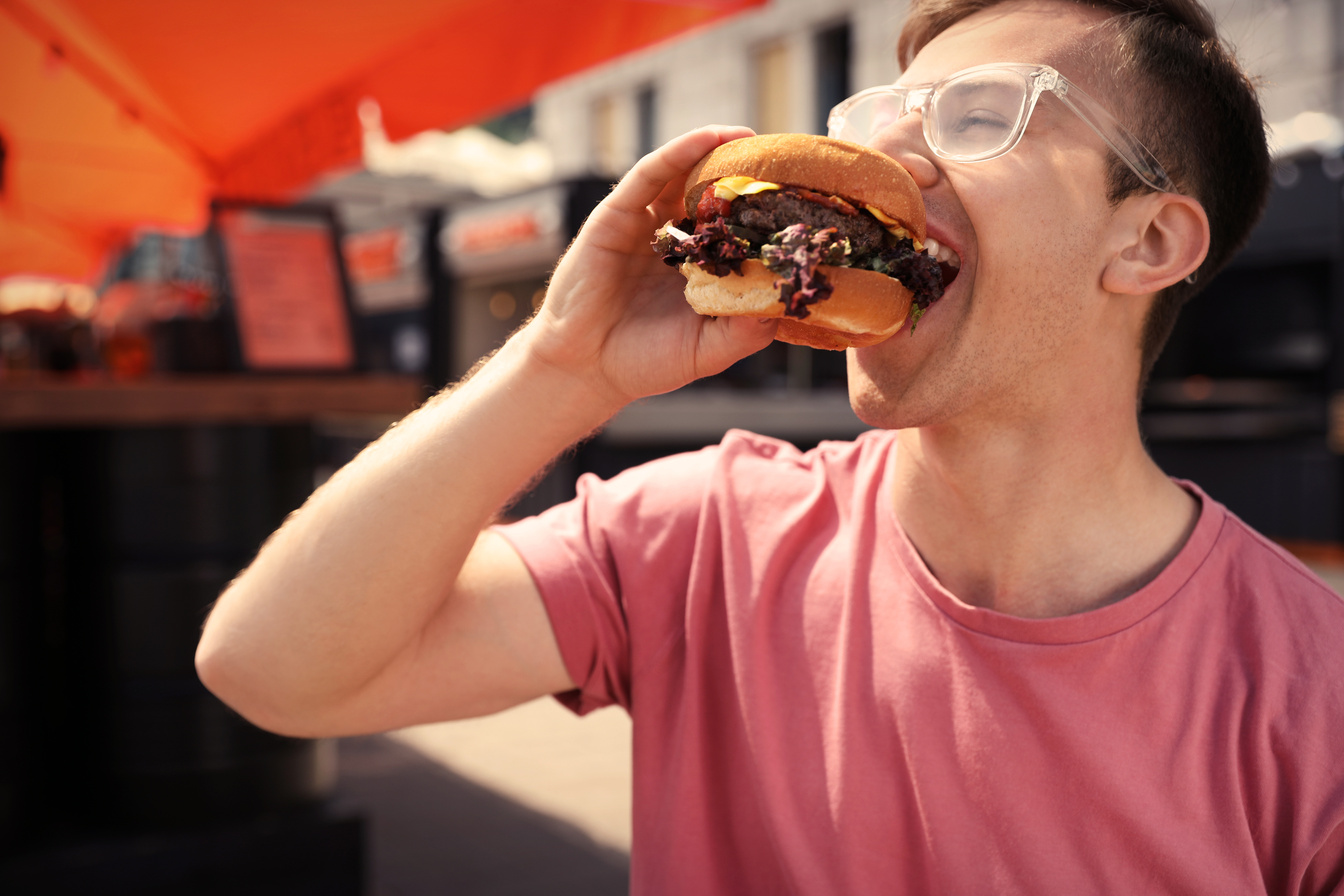 Young Man Eating Burger in Street Cafe